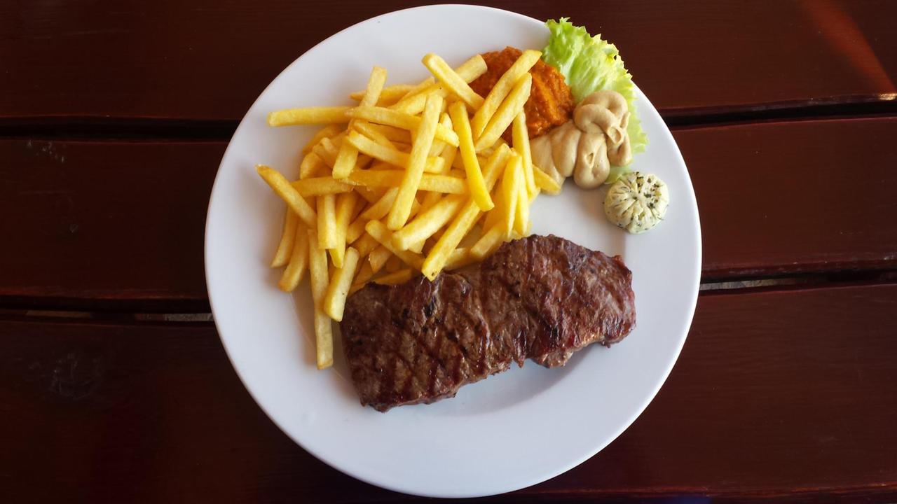 Ein Rumpsteak mit Pommes Frittes auf einem Teller. angerichtet mit Senf, Kräuterbutter und Paprikamus. Ein Rumpsteak mit Pommes Frittes auf einem Teller. angerichtet mit Senf, Kräuterbutter und Paprikamus.