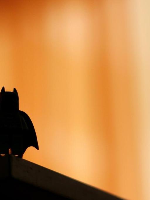 Die Silhouette einer Batman-Legofigur hebt sich dunkel vor einem unscharfen Bildhintergrund ab.