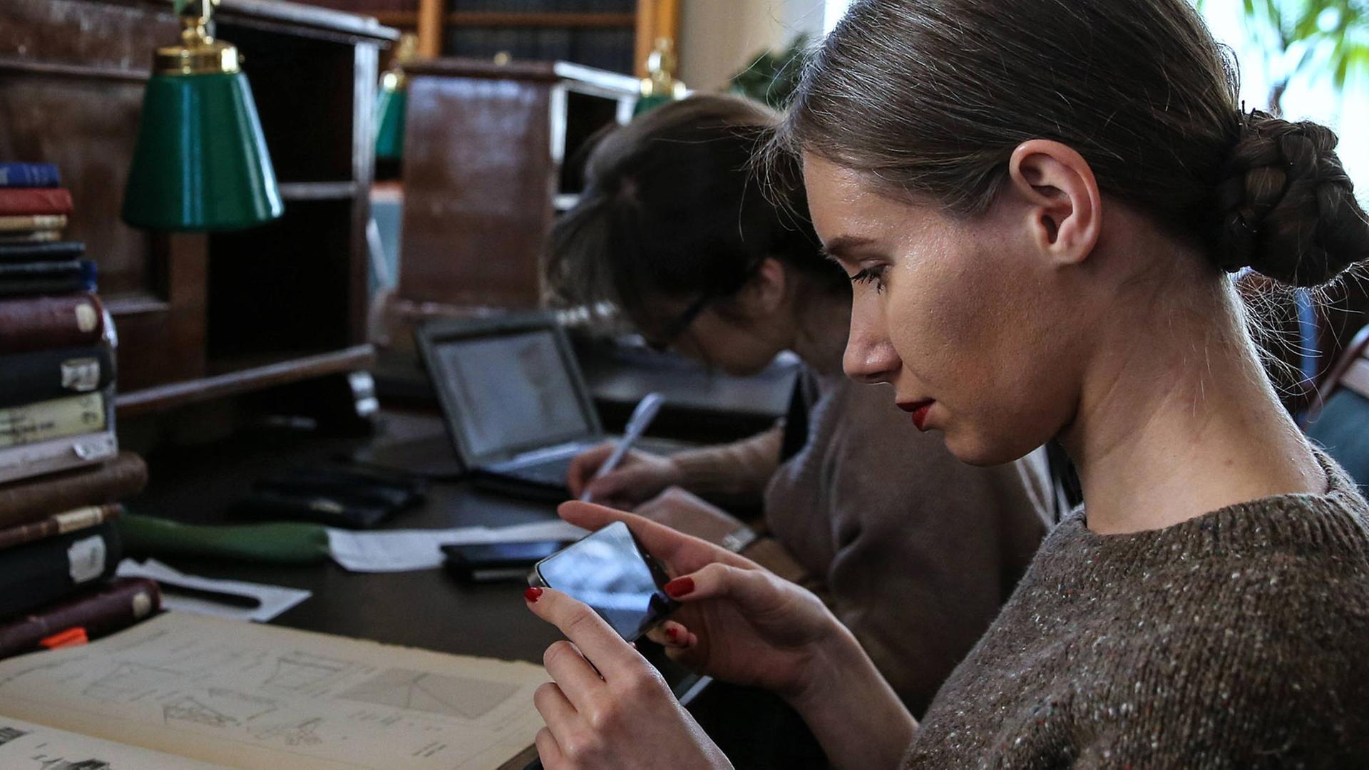 Eine Besucherin der russischen Staatsbibliothek macht in einem Lesesaal ein Foto mit einem Smartphone von Abbildungen in einem Buch Eine Besucherin der russischen Staatsbibliothek macht in einem Lesesaal ein Foto mit einem Smartphone von Abbildungen in einem Buch