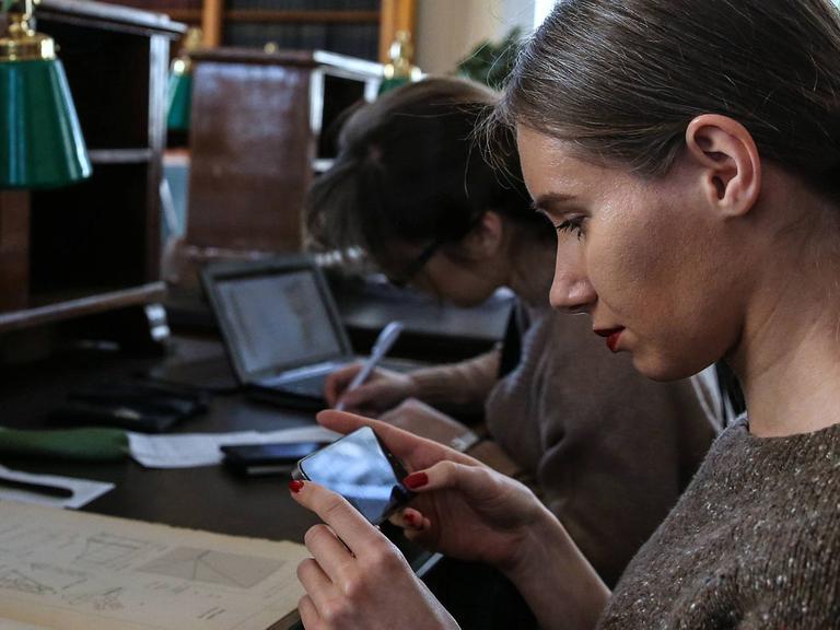 Eine Besucherin der russischen Staatsbibliothek macht in einem Lesesaal ein Foto mit einem Smartphone von Abbildungen in einem Buch