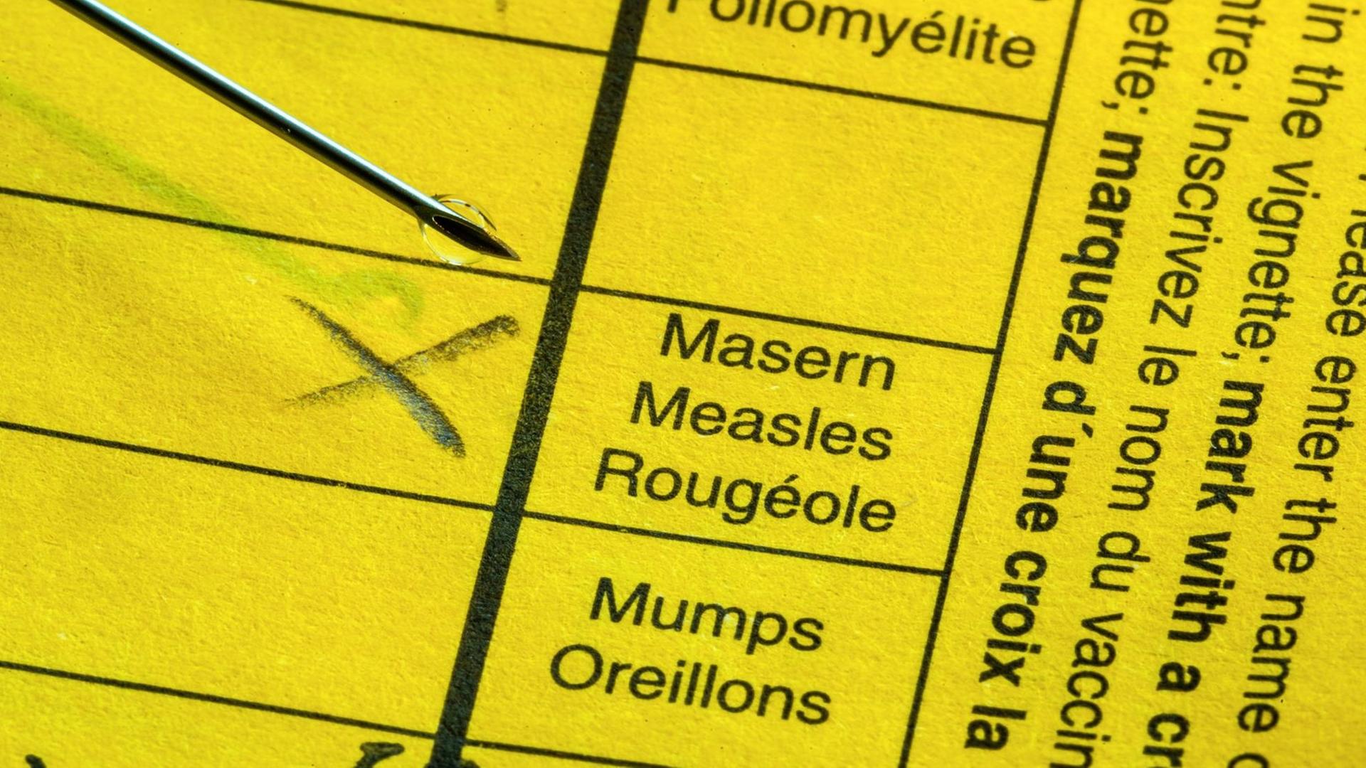 Ein gelber Impfpass mit Spritze: Bei "Masern" steht ein Kreuz. Ein gelber Impfpass mit Spritze: Bei "Masern" steht ein Kreuz.
