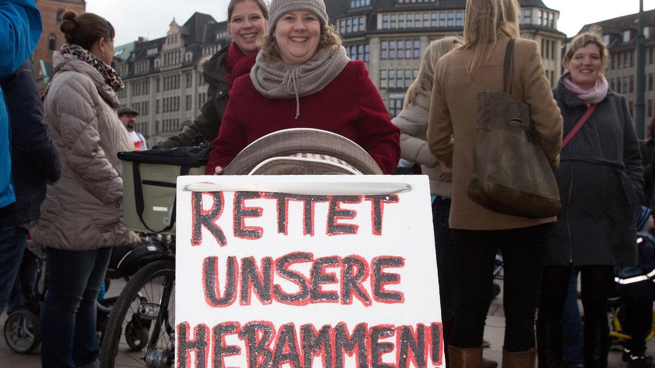 Eine Frau hält ein Schild mit der Aufschrift "Rettet unsere Hebammen" bei einer Demonstration hoch Eine Frau hält ein Schild mit der Aufschrift "Rettet unsere Hebammen" bei einer Demonstration hoch