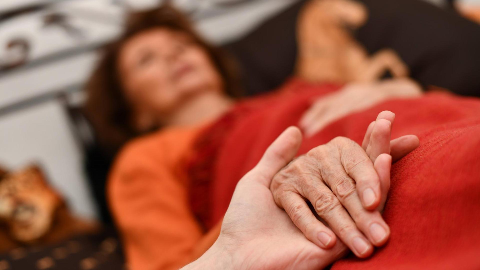 Alter Frau, die im Bett liegt, werden die Hände gehalten Alter Frau, die im Bett liegt, werden die Hände gehalten