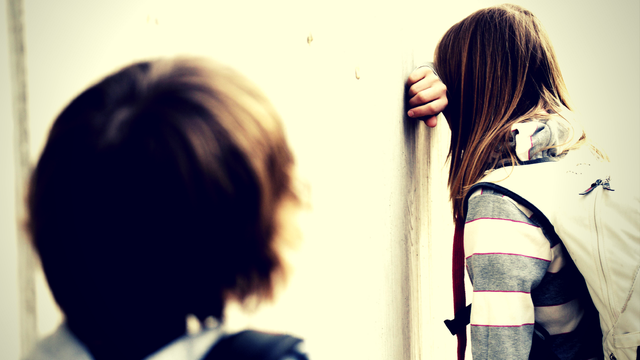 Ein Mädchen lehnt lehnt weinend an der Schulhauswand.