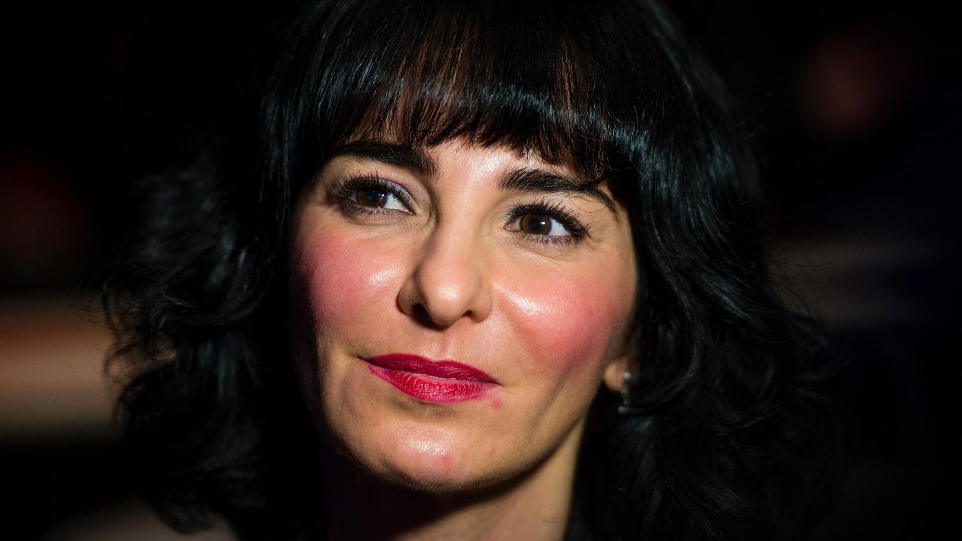 Porträt einer Frau mit schwarzen Haaren, sie trägt pinken Lippenstift und pinkes Rouge. Es handelt sich um die Schriftstellerin Mely Kiyak. Porträt einer Frau mit schwarzen Haaren, sie trägt pinken Lippenstift und pinkes Rouge. Es handelt sich um die Schriftstellerin Mely Kiyak.