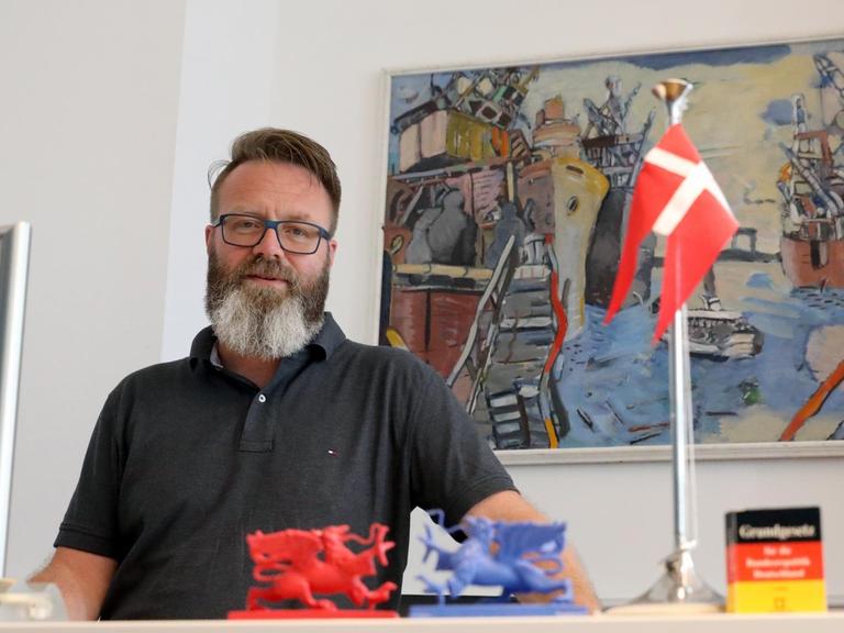 Der Däne Claus Ruhe Madsen, Oberbürgermeister von Rostock, sitzt an seinem Schreibtisch hinter einer dänischen Fahne.