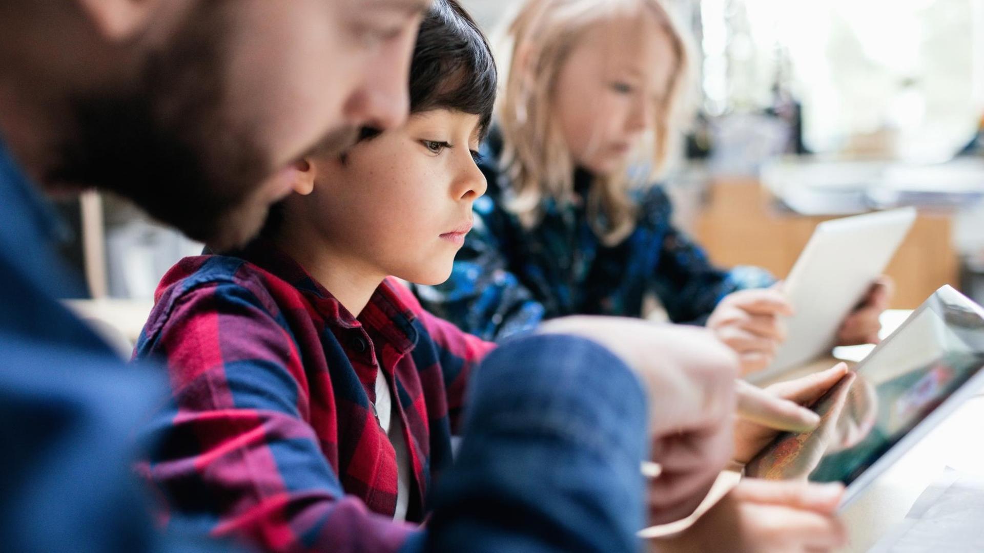 Aufnahme eines Lehrers, der einem Kind etwas am Tablet erklärt Aufnahme eines Lehrers, der einem Kind etwas am Tablet erklärt