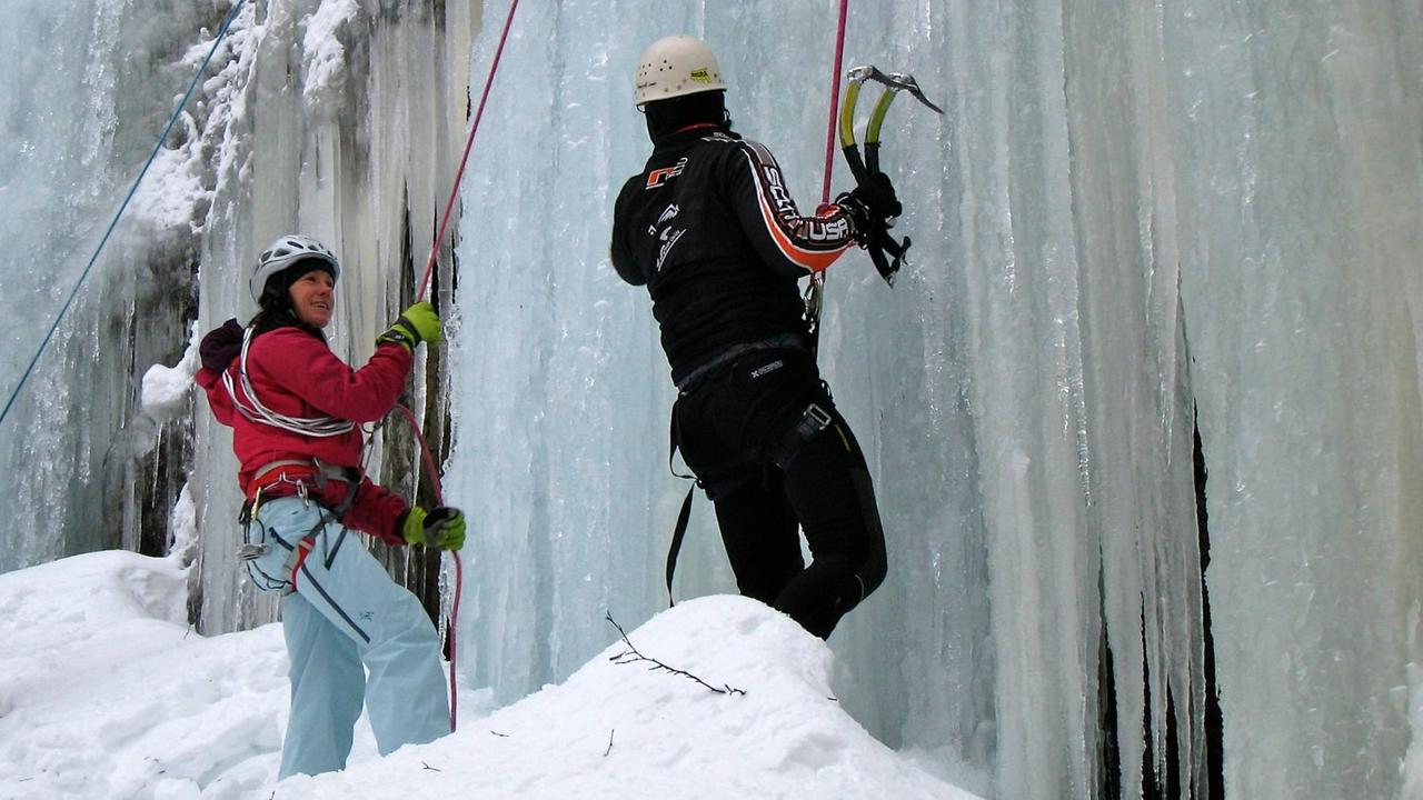 Ines Papert steht in roter Jacke und heller Hose an einer Eiswand im Pitztal in Österreich und spricht mit einem Teilnehmer beim Eiskletter-Workshop. Ines Papert steht in roter Jacke und heller Hose an einer Eiswand im Pitztal in Österreich und spricht mit einem Teilnehmer beim Eiskletter-Workshop.