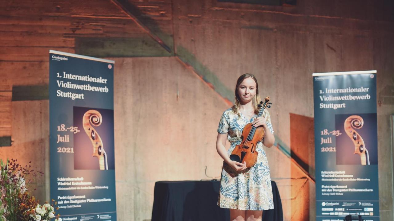 Musiker steht im kurzen Sommerkleid mit Instrument vor dem Wettbewerbsbanner Musiker steht im kurzen Sommerkleid mit Instrument vor dem Wettbewerbsbanner