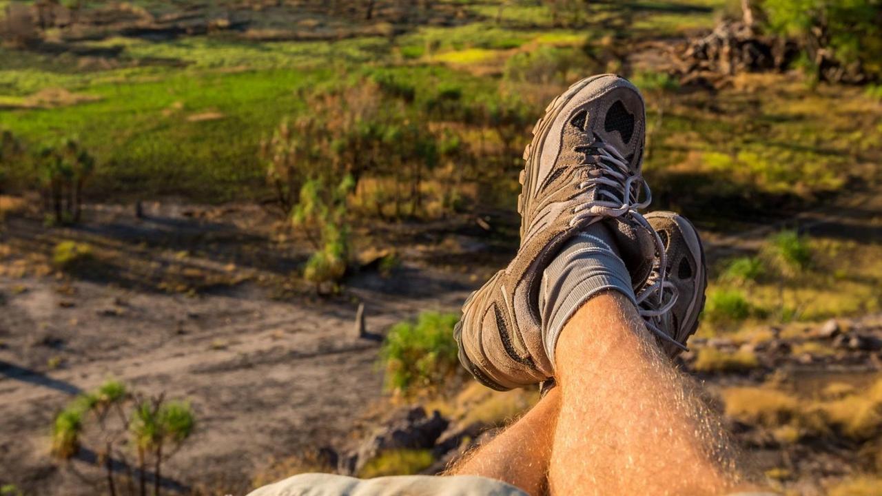 Ein Paar Männerbeine in Treckingschuhen, im Hintergrund die Nadab Floodplains in Australien. Ein Paar Männerbeine in Treckingschuhen, im Hintergrund die Nadab Floodplains in Australien.