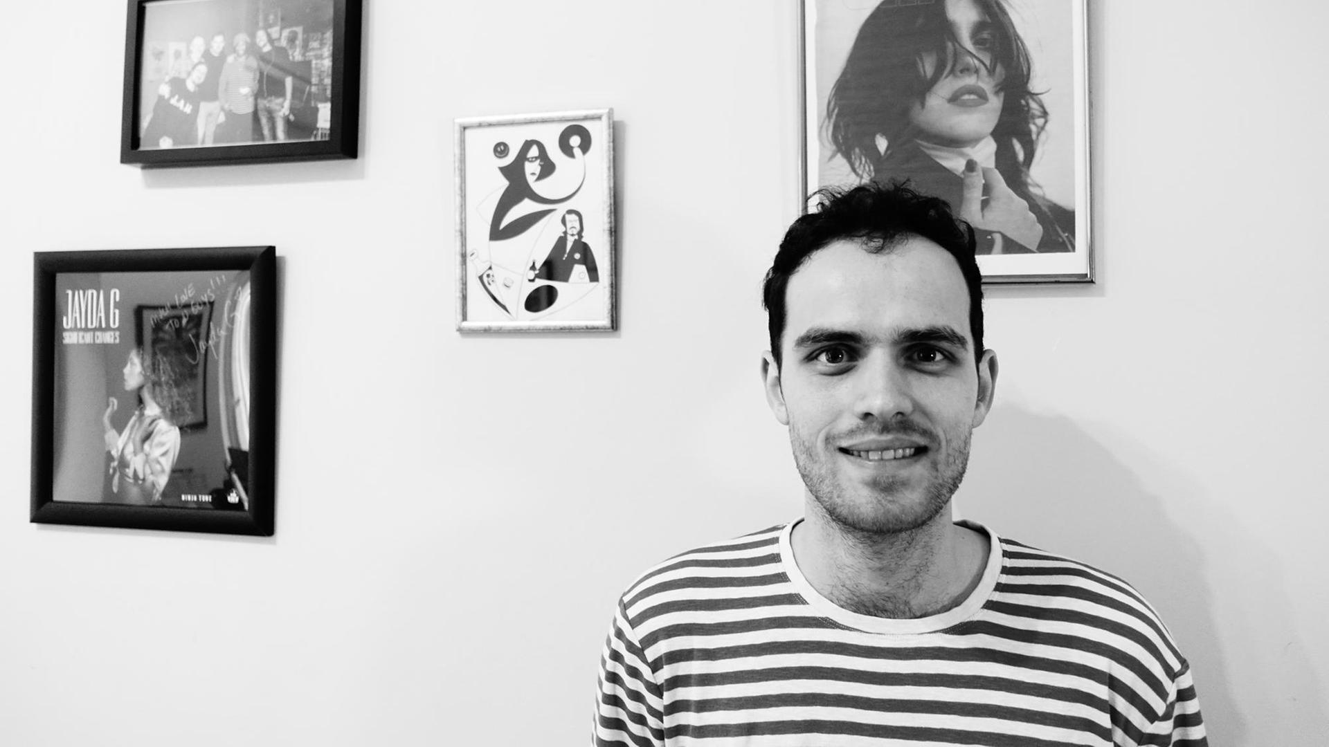 Der britische Musiker Jordan Rakei steht im gestreiften T-Shirt vor einer Wand mit Bilderrahmen