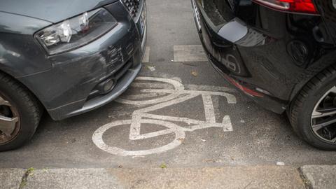 Zwischen der Front des einen und dem Heck des anderen Autos sieht man das weiss auf den Radweg gemalte Radfahrer-Zeichen.