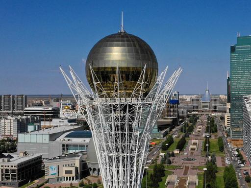 Luftansicht von Nur-Sultan in Kasachstan, futuristische Hochhäuser und im Vordergrund ein Monument mit großer goldener Kugel auf der Spitze