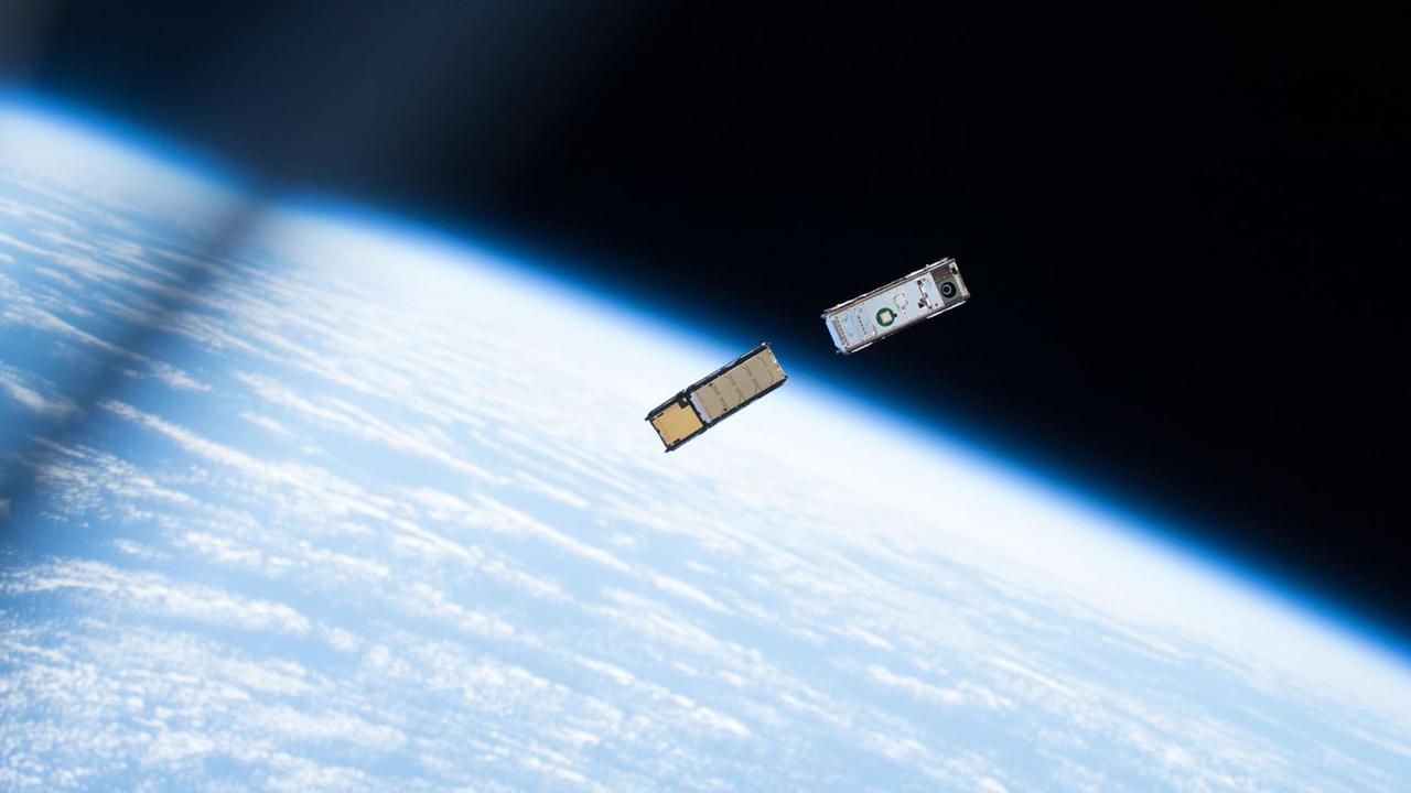 Mini-Satelliten, CubeSats, fliegen im All, im Hintergrund die Erde