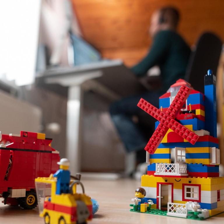 Ein Mann arbeitet im Homeoffice, während im Vordergrund Spielzeug seiner Kinder steht. 