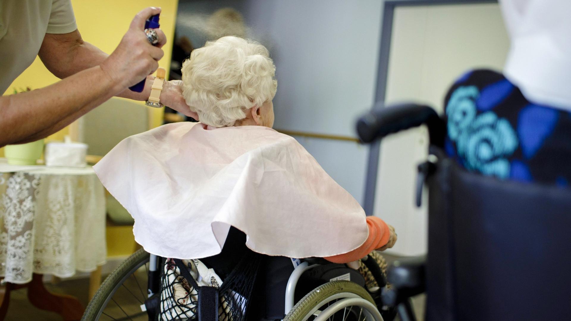 Eine Friseurin frisiert in einem eine alte Frau, die im Rollstuhl sitzt. Eine Friseurin frisiert in einem eine alte Frau, die im Rollstuhl sitzt.