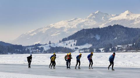 Eine Gruppe Eisläufer auf dem Weissensee vor Alpenpanorama