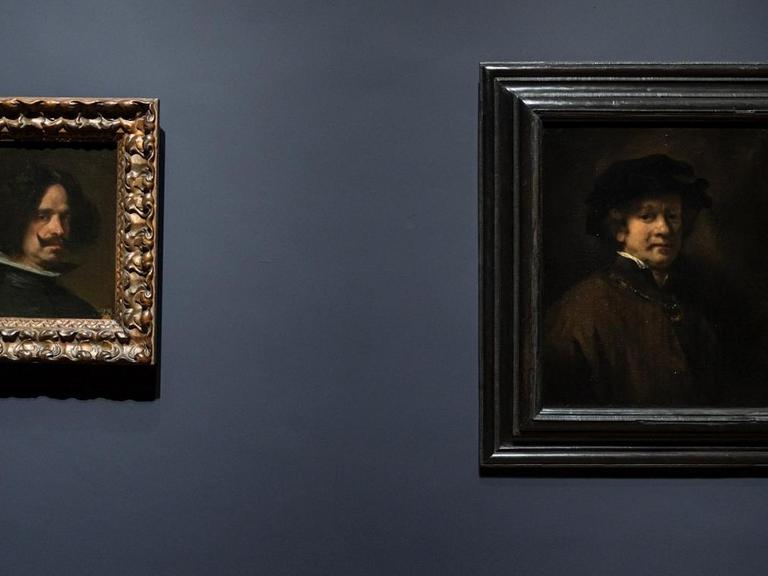 Blick in die Austellung. Zwei Selbstportäts von Rembrandt und Velázquez hängen nebeneinander an einer dunkelblauen Wand.
