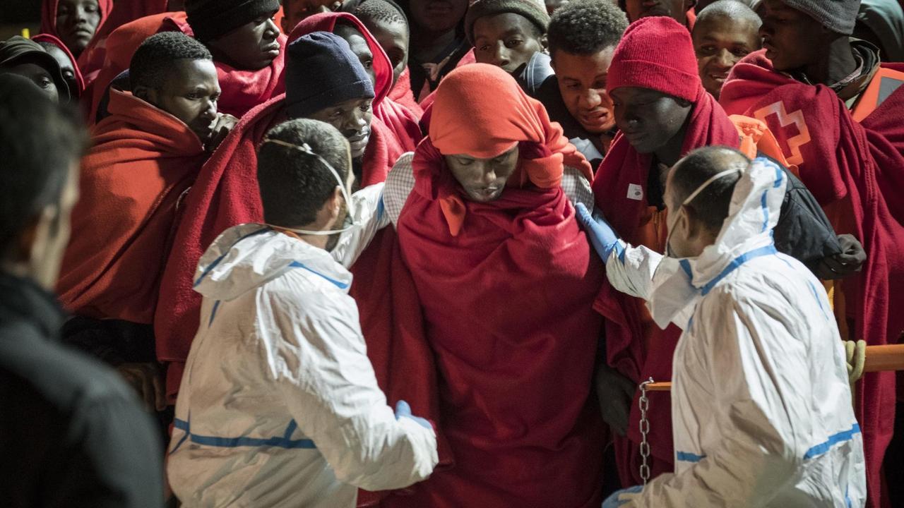 Mitarbeiter des Roten Kreuzes mit Atemschutzmasken empfangen aus Seenot gerettete Migranten am Hafen von Málaga. Mitarbeiter des Roten Kreuzes mit Atemschutzmasken empfangen aus Seenot gerettete Migranten am Hafen von Málaga.