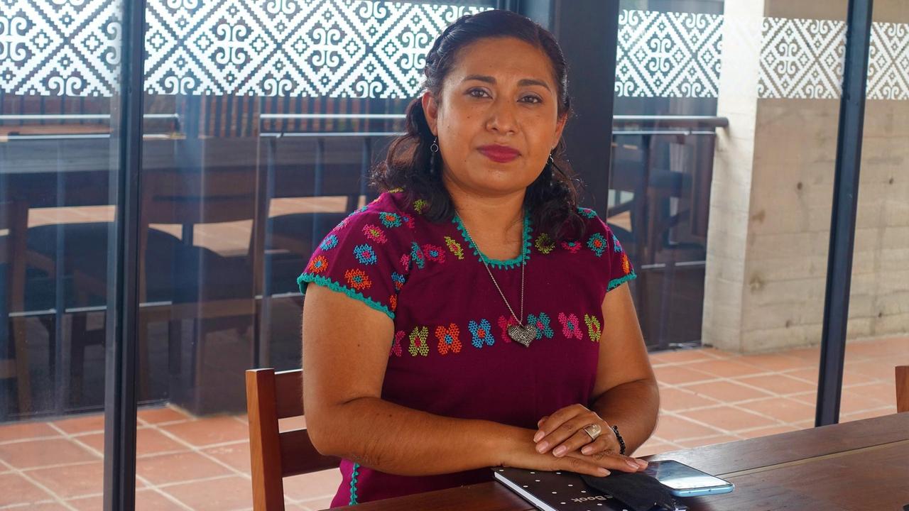Patricia Cruz vom Instituto de Artesania, kümmert sich um die Vermarktung von Kunsthandwerk. Sie sitzt am Tisch und trägt traditionelle rote Oberbekleidung.