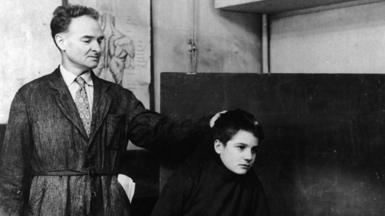 Filmszene aus "Sie küßten und sie schlugen ihn", 1958. Ein Lehrer bestraft einen Schüler, der an der Tafel steht. Filmszene aus "Sie küßten und sie schlugen ihn", 1958. Ein Lehrer bestraft einen Schüler, der an der Tafel steht.