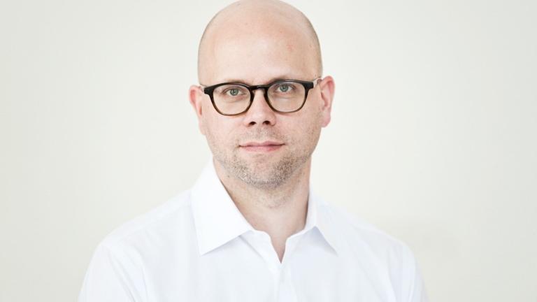 Ein Mann mit weißem Hemd und dunkler Brille schaut freundlich in die Kamera. Es ist Clemens Stachel. Ein Mann mit weißem Hemd und dunkler Brille schaut freundlich in die Kamera. Es ist Clemens Stachel.