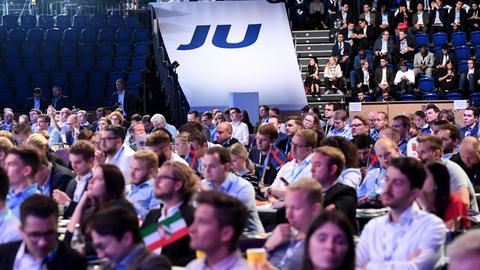 Blick von vorne auf die Delegierten in der Halle; im Hintergrund ein weißes "JU"-Banner.