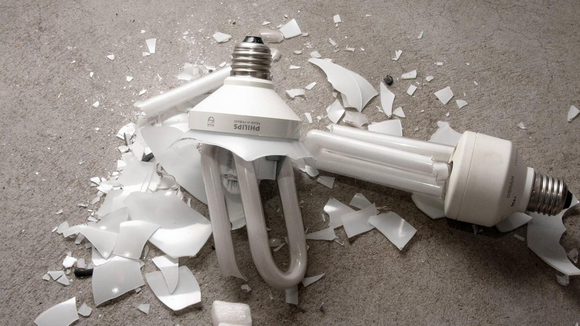 Zwei zerbrochene Energiesparlampen liegen auf einem grauem Boden Zwei zerbrochene Energiesparlampen liegen auf einem grauem Boden
