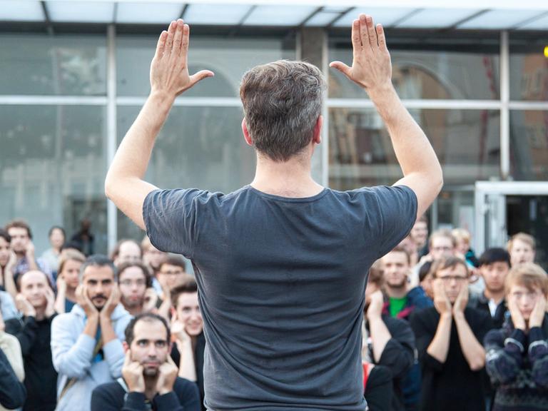 Ein Mann animiert das Publikum, Gesten und Laute nachzumachen