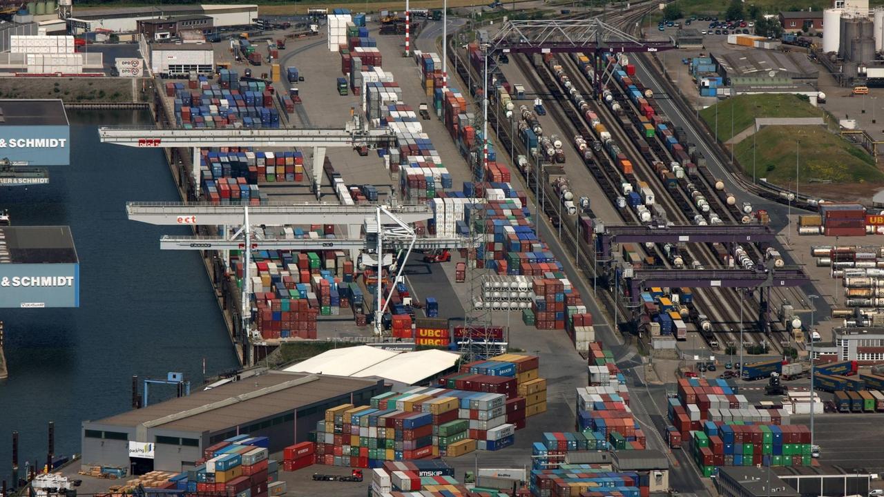 Eine Luftaufnahme des Duisburger Hafens zeigt zahlreiche Container, Kräne, den Hafen und den Bahnhof, an dem die Güterzüge halten.
Eine Luftaufnahme des Duisburger Hafens zeigt zahlreiche Container, Kräne, den Hafen und den Bahnhof, an dem die Güterzüge halten.