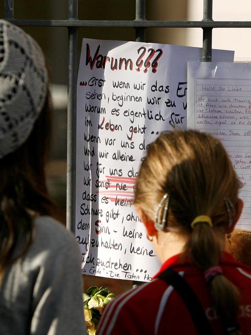 Jugendliche betrachten an einem Schultor einen Zettel mit dem Titel "Warum???"