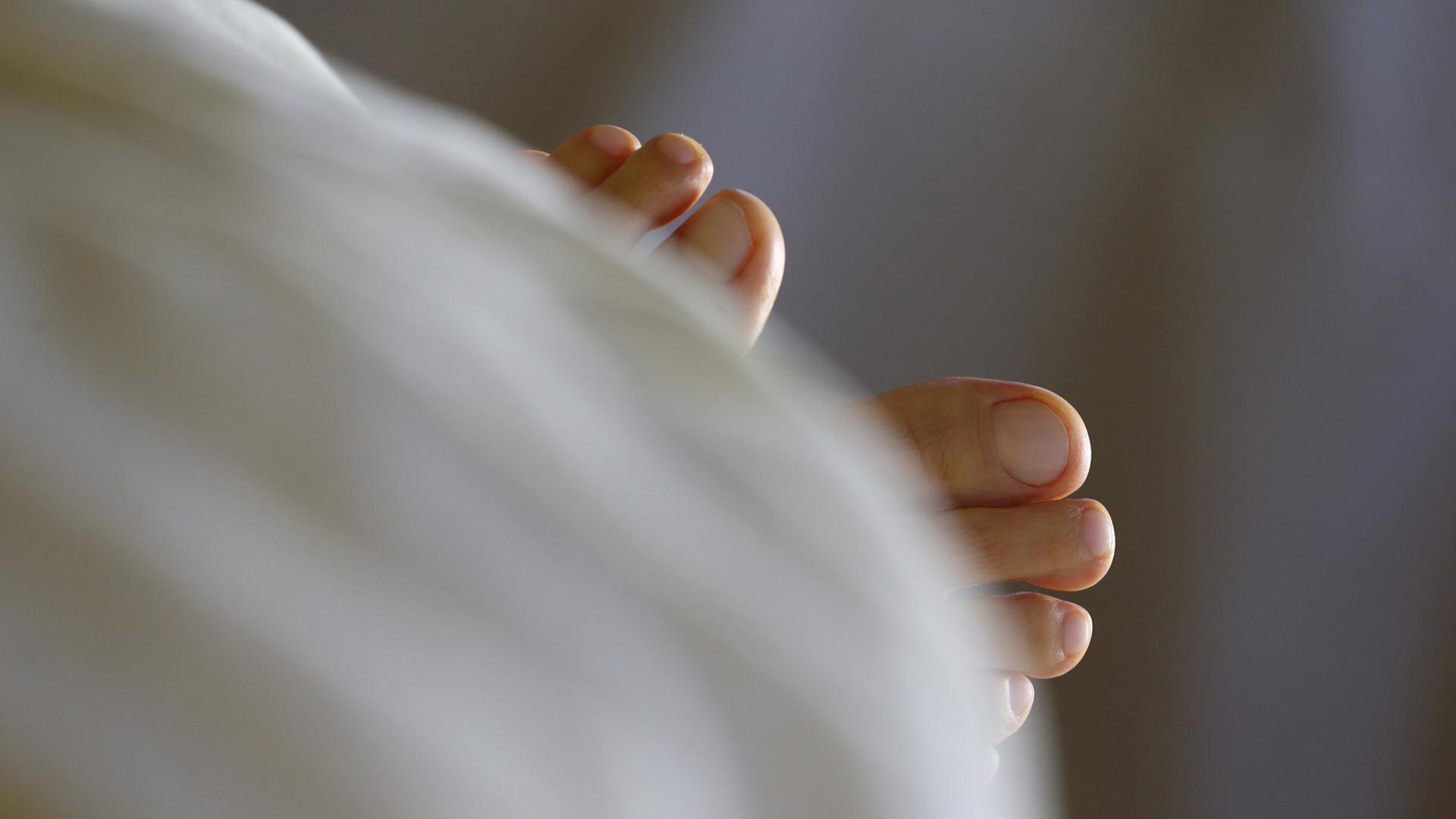 Unter einer Bettdecke schauen die beiden Füße einer schlafenden Frau heraus. Unter einer Bettdecke schauen die beiden Füße einer schlafenden Frau heraus.