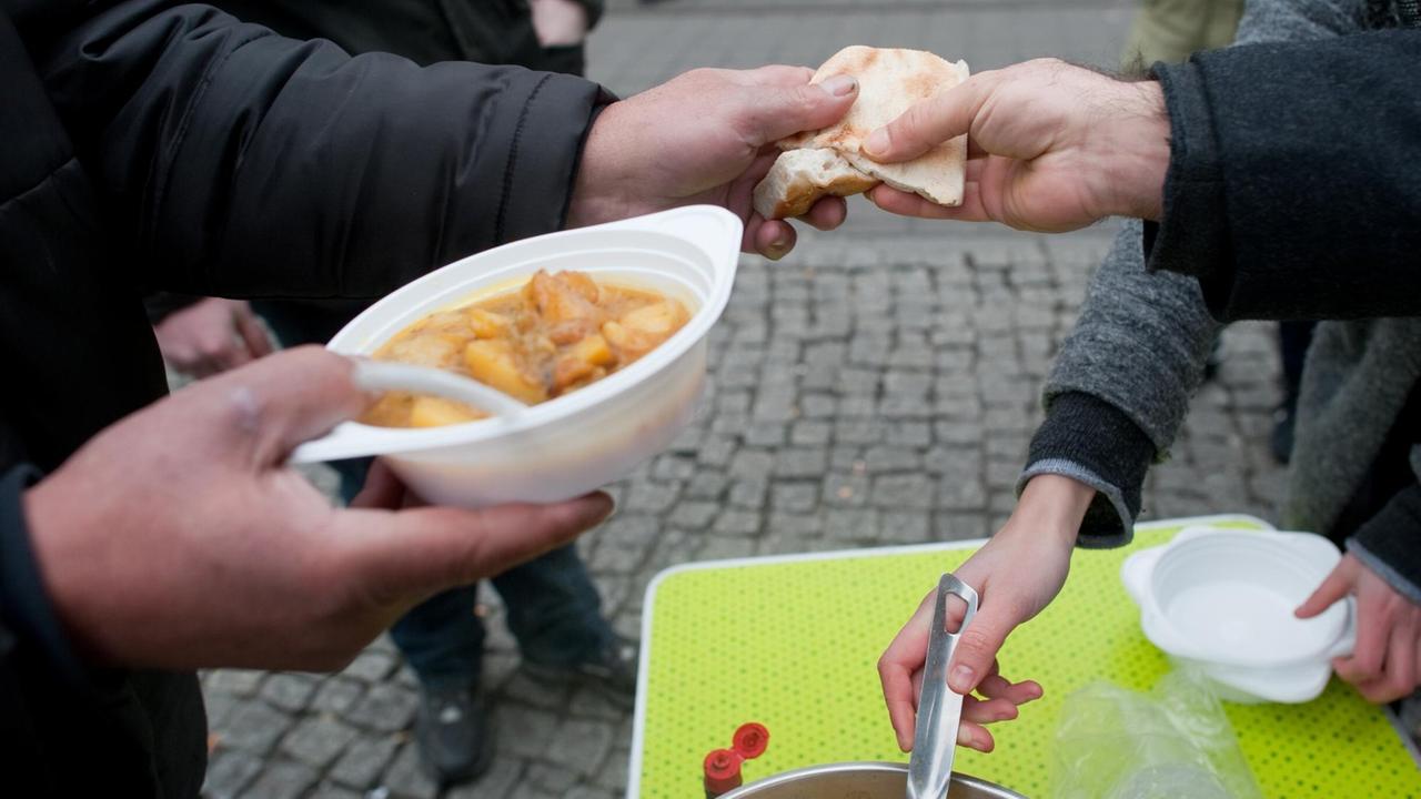 Man sieht die Hände von Menschen, einen Teller Suppe und ein Stück Brot. Man sieht die Hände von Menschen, einen Teller Suppe und ein Stück Brot.