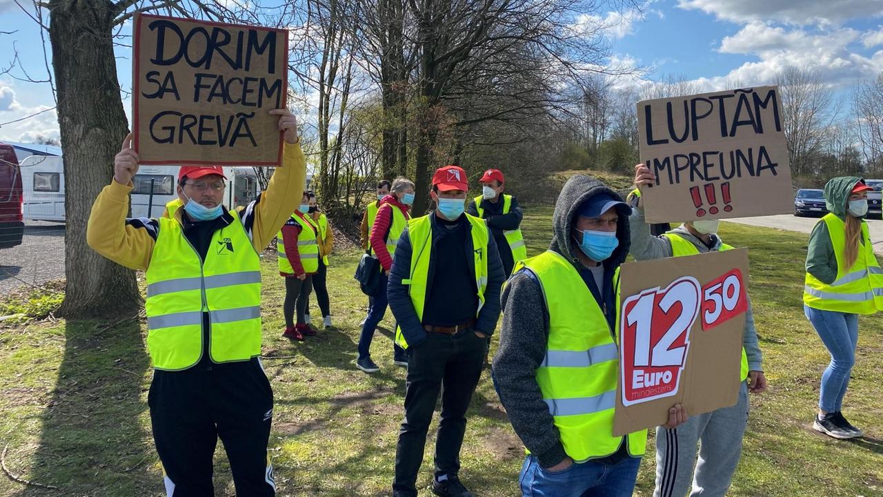 Arbeiter stehen mit Protestplakaten auf einer Wiese vor einem Werk. Arbeiter stehen mit Protestplakaten auf einer Wiese vor einem Werk.