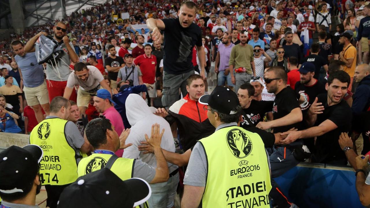 Ordner in leuchtgelben Warnwesten versuchen, die Hooligans von der Tribüne herunterzusteuern. Ordner in leuchtgelben Warnwesten versuchen, die Hooligans von der Tribüne herunterzusteuern.