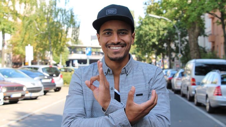 Ein junger Mann mit Basecap steht auf einer Straße und lacht in die Kamera. Ein junger Mann mit Basecap steht auf einer Straße und lacht in die Kamera.