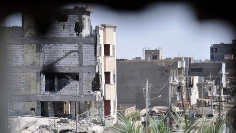 Ein Foto durch ein Loch in einer Mauer zeigt am 24.06.2014 Gebäude in der Stadt Ramadi, die bei Kämpfen zwischen sunnitischen Milizen und Regierungsgegnern, inklusive der Gruppe ISIS, beschädigt wurden.
