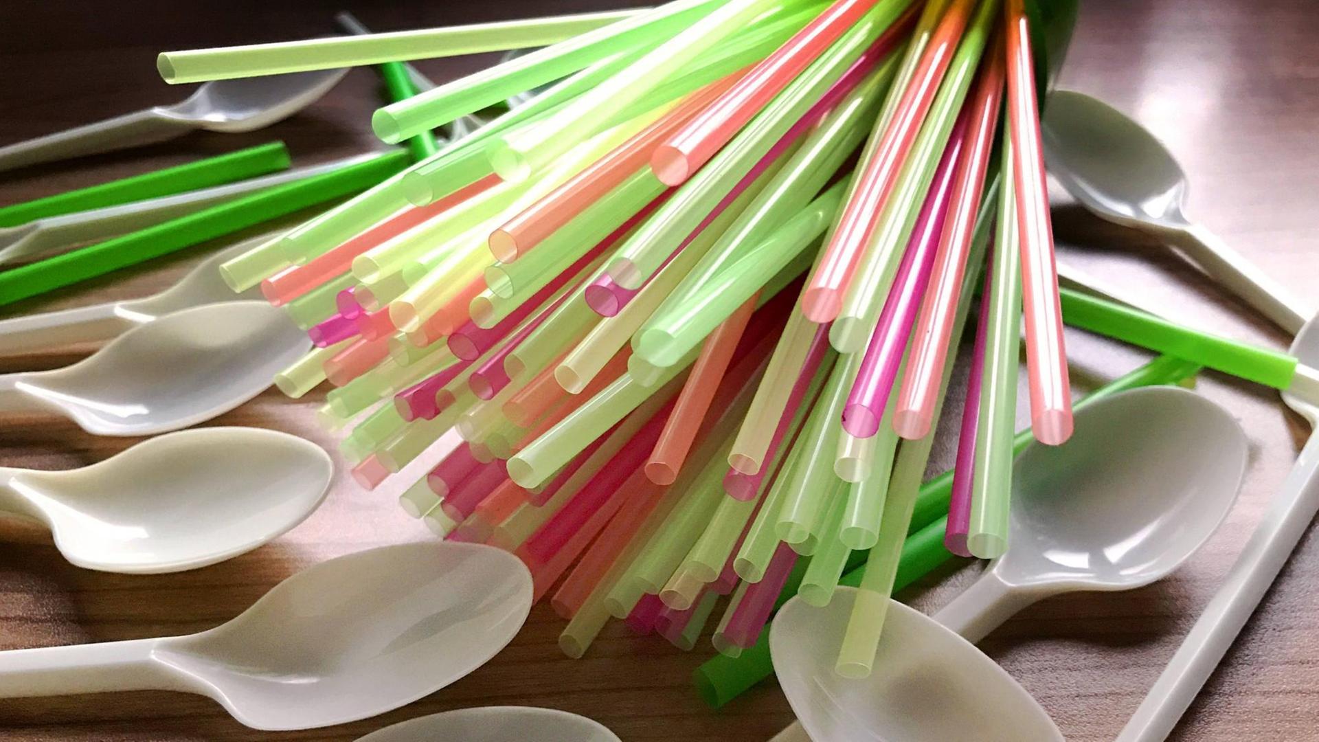 Bunte Trink-Halme und Einweg-Löffel aus Plastik liegen auf einem Tisch. Bunte Trink-Halme und Einweg-Löffel aus Plastik liegen auf einem Tisch.