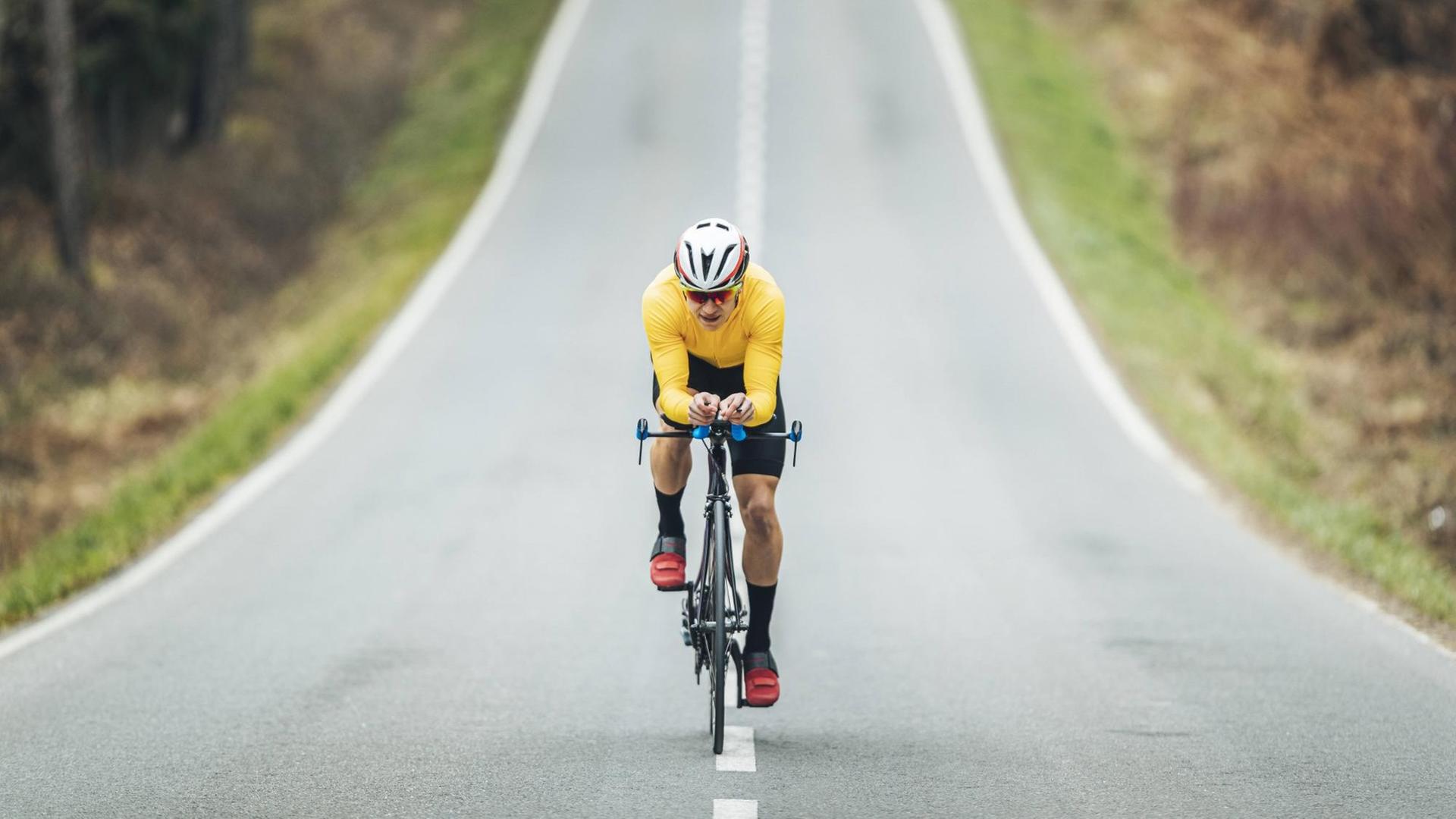 Ein Mann mit gelbem Shirt und Fahrradhelm fährt auf einer asphaltierten Strasse Rennrad Ein Mann mit gelbem Shirt und Fahrradhelm fährt auf einer asphaltierten Strasse Rennrad