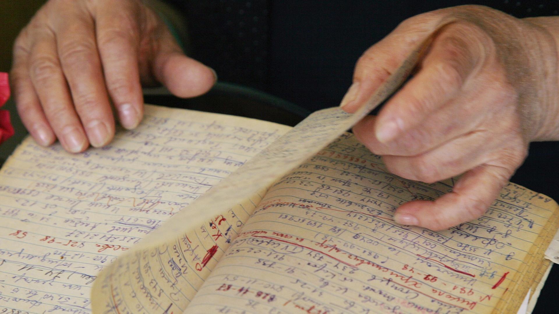 Eine ältere Frau blättert in einem Notizbuch - ihre Hände sind zu sehen. Eine ältere Frau blättert in einem Notizbuch - ihre Hände sind zu sehen.