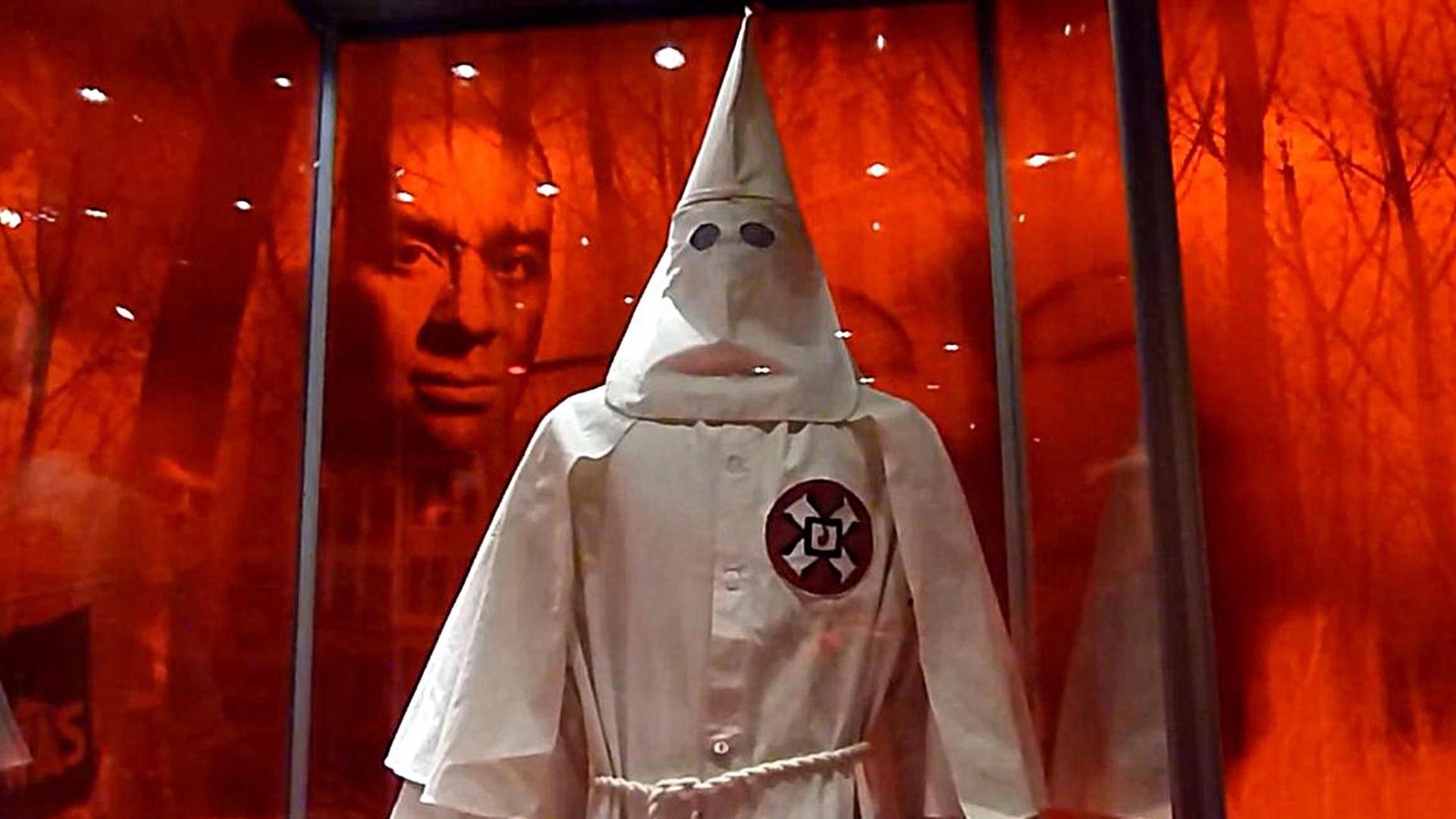 Die Robe eines Ku-Klux-Klan-Mitglieds, dahinter das Gesicht eines Schwarzen in einer Ausstellung in Washington. Die Robe eines Ku-Klux-Klan-Mitglieds, dahinter das Gesicht eines Schwarzen in einer Ausstellung in Washington.