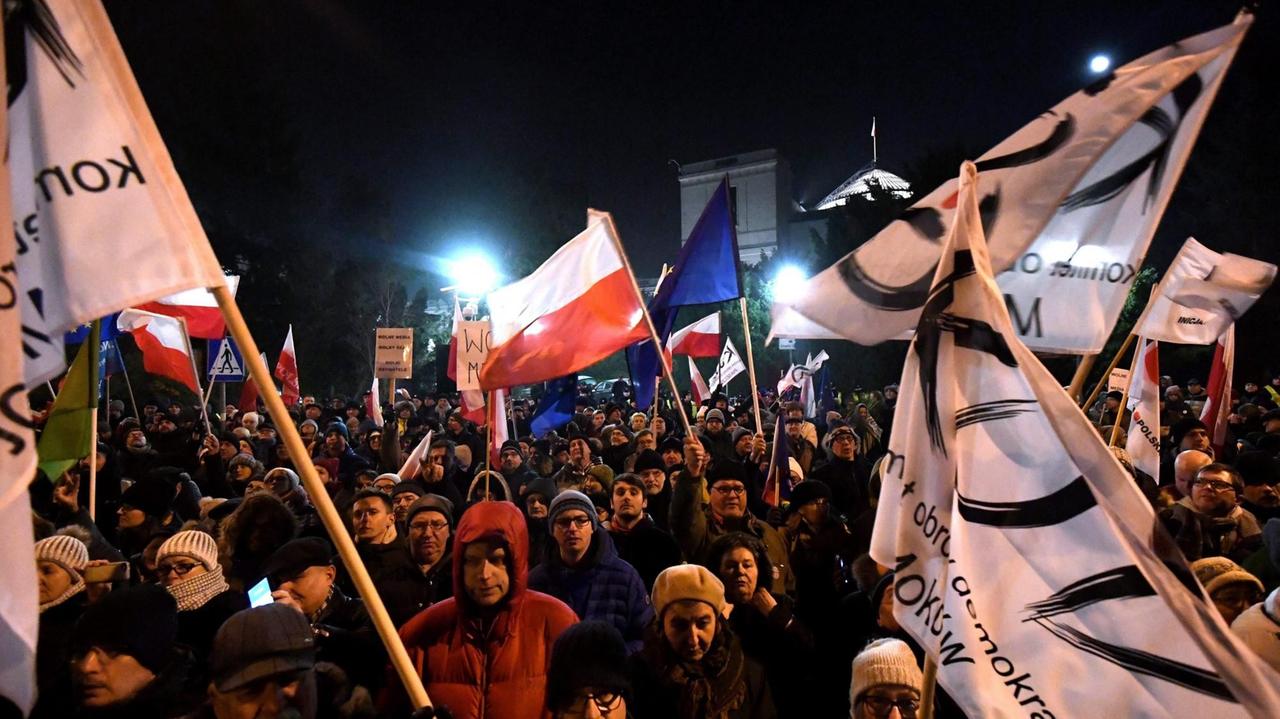 Eine Gruppe von Demonstranten steht im Dunkeln vor dem polnischen Parlament und schwenkt Fahnen.