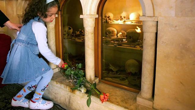 Ein amenisches Kind legt in einer Kirche im Libanon eine Rose vor einem Schrein mit Totenköpfen der Opfer nieder.