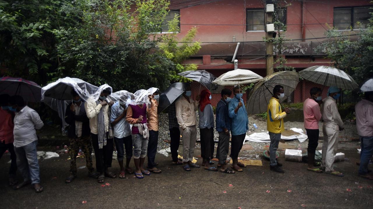 Indische Wanderarbeiter stehen für einen Coronatest Schlange im Regen. 