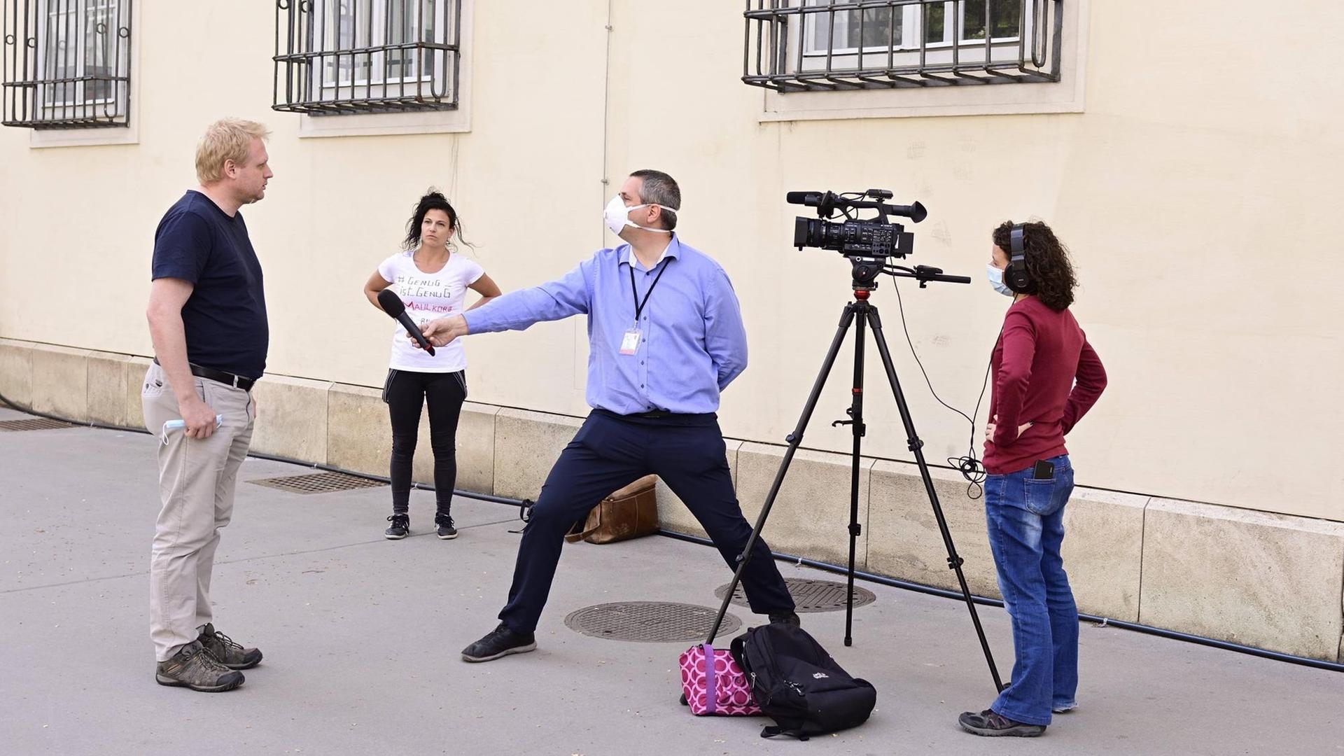 Ein Reporter streckt sein Mikrofon mit dem Arm weit von sich in Richtung Interviewpartner, um den coronabedingten Sicherheitsabstand zu wahren