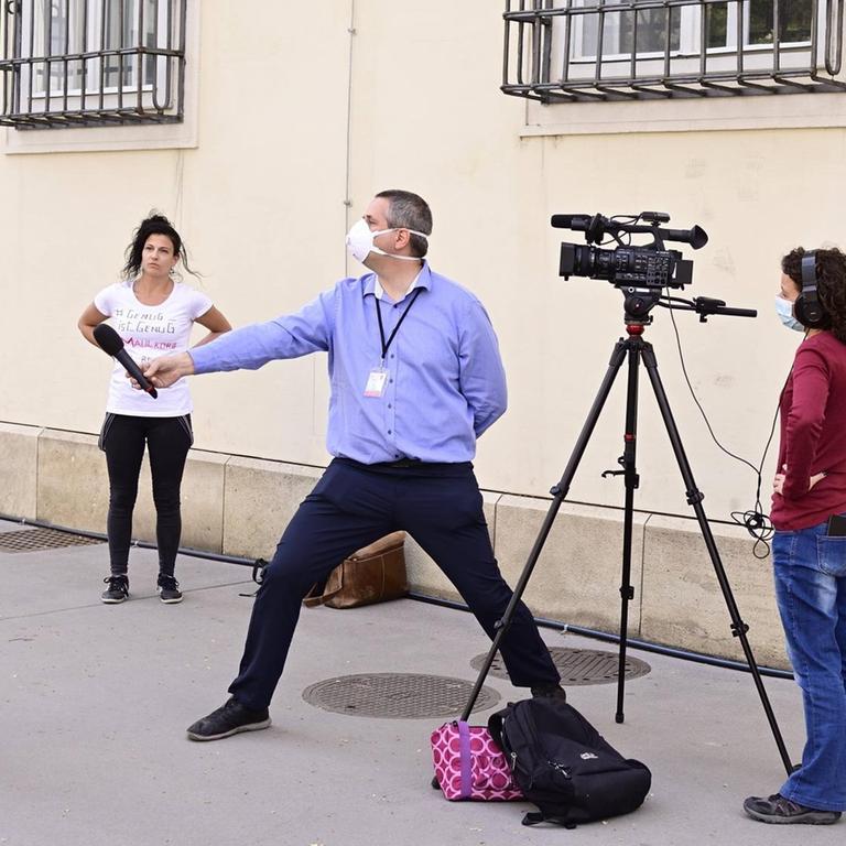 Ein Reporter streckt sein Mikrofon mit dem Arm weit von sich in Richtung Interviewpartner, um den coronabedingten Sicherheitsabstand zu wahren