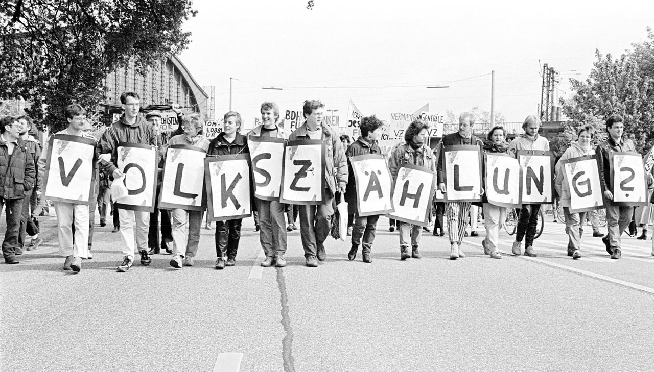 Das Schwarz-weiß-Foto aus den 1980er-Jahren zeigt Demonstrierende, die in einer Reihe nebeneinander laufen. Jeder trägt ein Schild mit einem Buchstaben vor sich, sodass sich am Ende der Schriftzug "VOLKSZÄHLUNG?" ergibt.