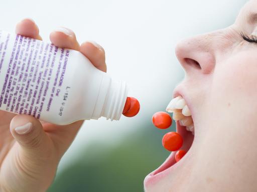 Eine Frau schüttet sich rote Pillen in den Mund.