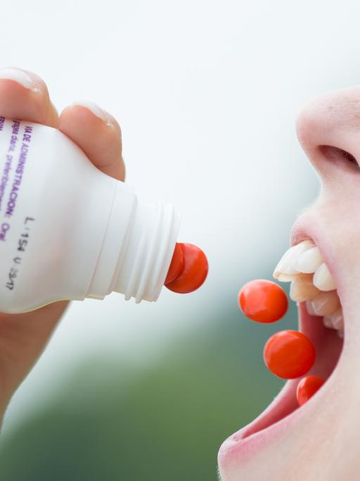 Eine Frau schüttet sich rote Pillen in den Mund.