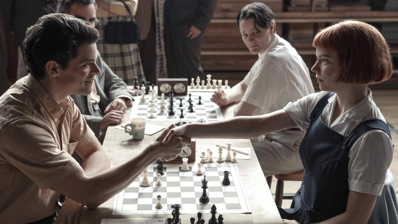 Szene aus der Netflix-Serie "Das Damengambit". Ein Mann und eine Frau sitzen vor einem Schachbrett und begrüßen sich. Szene aus der Netflix-Serie "Das Damengambit". Ein Mann und eine Frau sitzen vor einem Schachbrett und begrüßen sich.